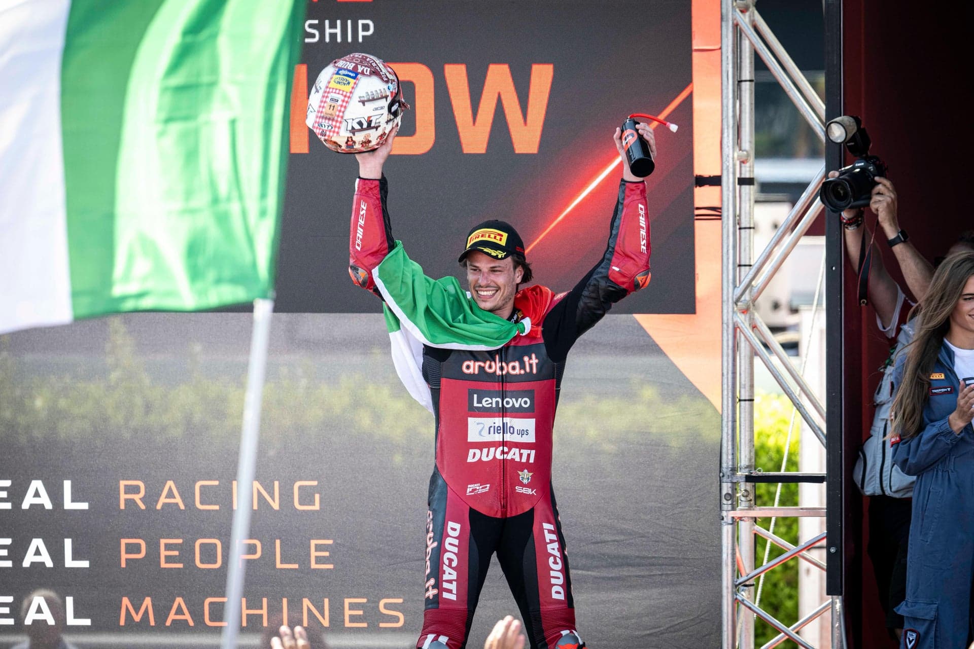 Nicolò Bulega sul podio con la bandiera italiana e il casco speciale al Misano World Circuit 2026